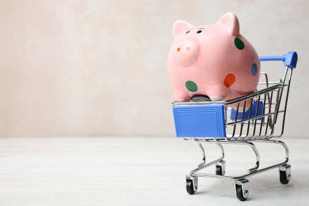 Pink pig piggy bank in polka dot in grocery trolly on wooden table on neutral background. Copy space. Concept shopping. - Fotografie, Obrázek