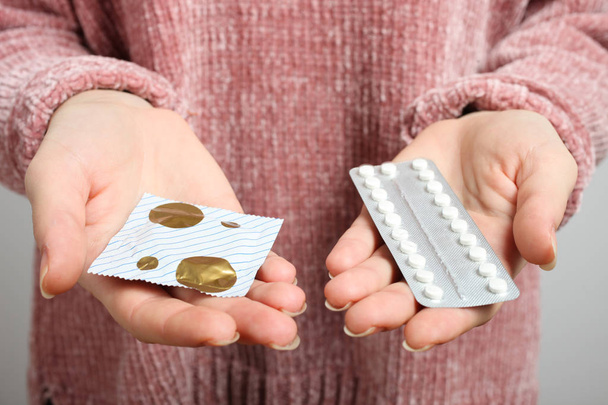 Woman holding in hands oral contraceptive pills and condom, choice. Concept gynecology, sex education. - Photo, Image