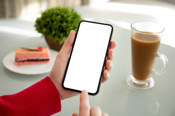 female hands holding phone with isolated screen above the table in a cafe - Фото, изображение