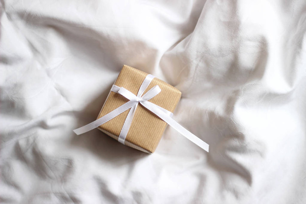 Present box for holidays, decorated with white ribbon bow. Valentine's Day gift, International Women's Day gift over white bed linen background. - Valokuva, kuva
