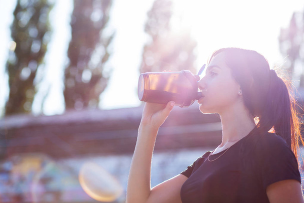 Closeup shot of sporty woman drinking water in soft evening backlight. Space for text - Foto, afbeelding