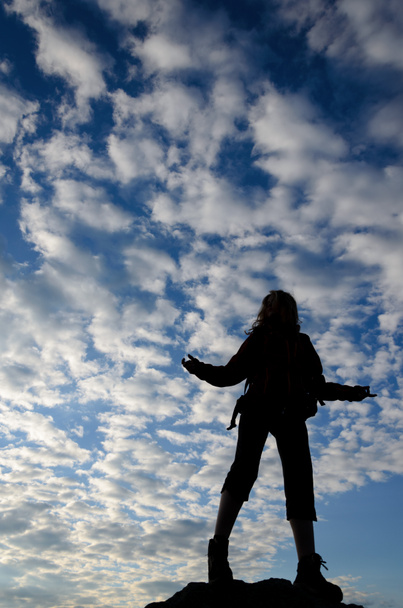 Expressieve silhouet van een jonge vrouw in een bewolkte hemelachtergrond. - Foto, afbeelding