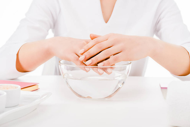 Vue recadrée de manucure tenant les mains au-dessus du bain de main en verre isolé sur blanc
 - Photo, image