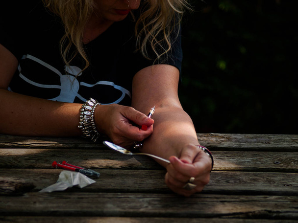 Una mujer inyectándose droga en el brazo con una jeringa
 - Foto, Imagen