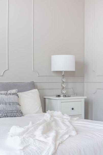 Lâmpada branca na mesa de cabeceira de madeira ao lado da cama king size, espaço da cópia na parede vazia cinzenta
 - Foto, Imagem