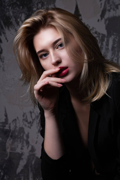 Elegant blonde model with perfect skin wearing black jacket posing at studio with shadows - Fotoğraf, Görsel