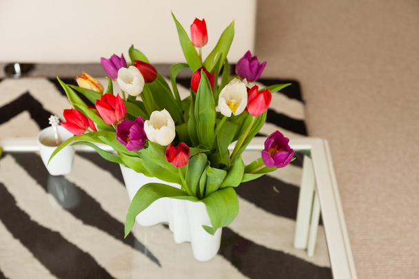 Цветные тюльпаны в белой вазе на столе в гостиной
. - Фото, изображение