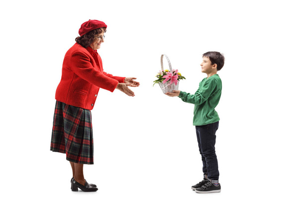 Plan complet d'un jeune garçon donnant un panier avec des fleurs à sa grand-mère isolée sur fond blanc
 - Photo, image