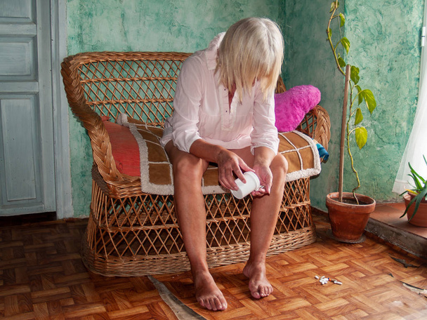 Ανώτερος γυναίκα με πολλά χάπια στο χέρι των διαφορετικών χρωμάτων και μεγεθών, κάθεται σε έναν καναπέ - Φωτογραφία, εικόνα