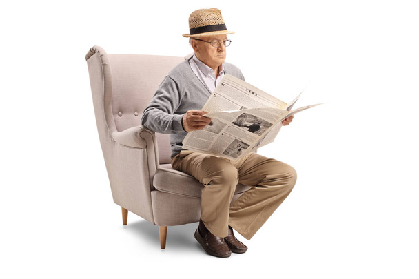 Senior man sitting in an armchair and reading a newspaper isolated on white background - Fotoğraf, Görsel