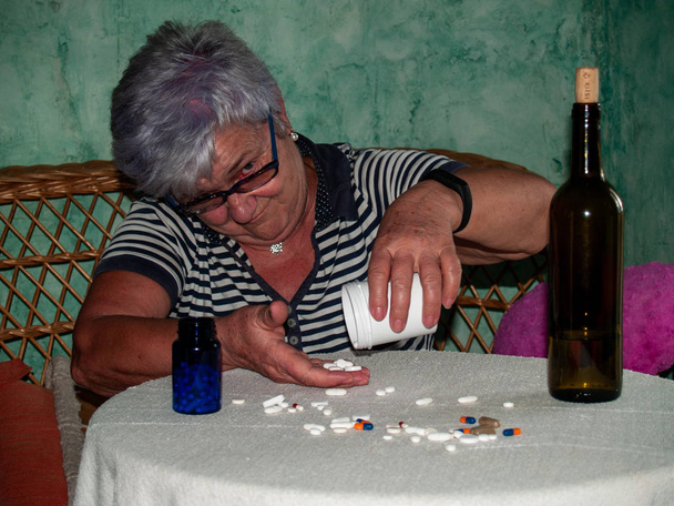 Uma mulher sênior com uma garrafa de vinho e um grande número de pílulas em sua mão de diferentes cores e tamanhos
 - Foto, Imagem