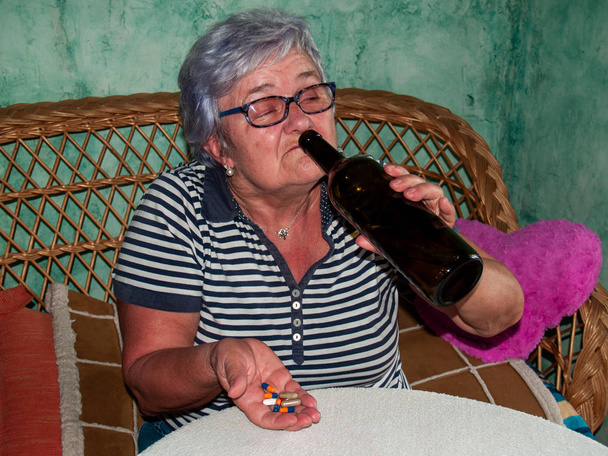 Senior kobiety z butelką wina oraz dużą liczbę tabletek w ręce różnych kolorach i rozmiarach - Zdjęcie, obraz