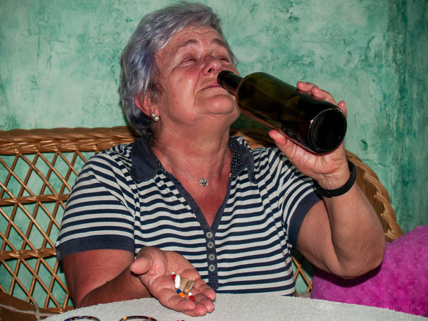 Vanhempi nainen pullo viiniä ja suuri määrä pillereitä kädessään eri värejä ja kokoja
 - Valokuva, kuva
