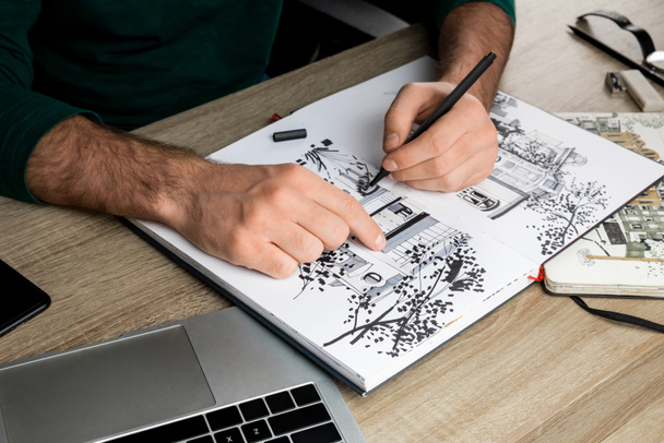 selective focus of mans hands drawing in album on wooden table next to laptop - Photo, Image