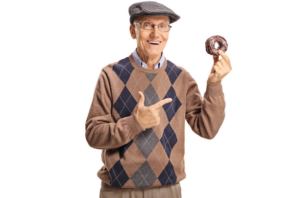 Cheerful senior man holding a chocolate donut and pointing at it isolated on white background - Фото, изображение