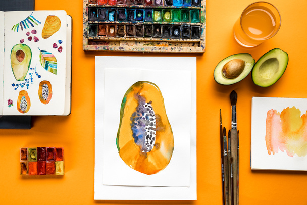 top view of papaya drawings next to colored paints and paintbrushes on yellow background  - Foto, Bild