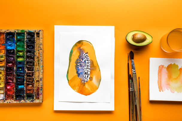 top view of album with papaya drawing next to colored paints and paintbrushes   on yellow background  - 写真・画像