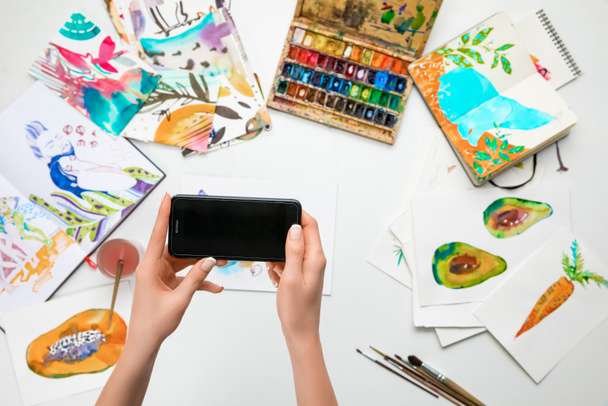 mise au point sélective des mains féminines faisant photo de peintures à l'aquarelle et d'ustensiles de dessin à l'aide d'un smartphone
 - Photo, image