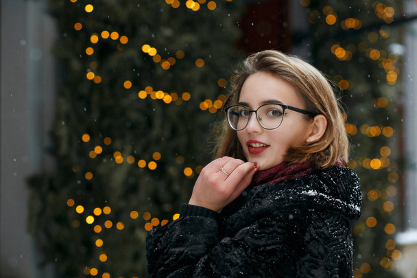 Verheugd brunette vrouw bril poseren tegen slingers op de straat. Lege ruimte - Foto, afbeelding