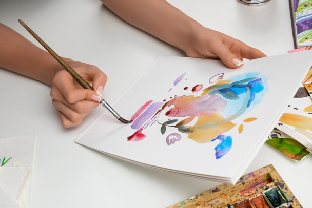 selektiver Fokus weiblicher Hände beim Malen mit Aquarellfarben und Pinsel auf weißem Papier - Foto, Bild