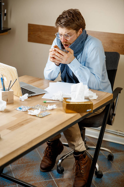 Feeling sick and tired. The man with cup of hot tea working in office, businessman caught cold, seasonal flu. Pandemic influenza, disease prevention, air conditioning in office cause sickness - Fotoğraf, Görsel