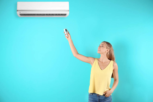Young woman turning on air conditioner against color background - Фото, зображення