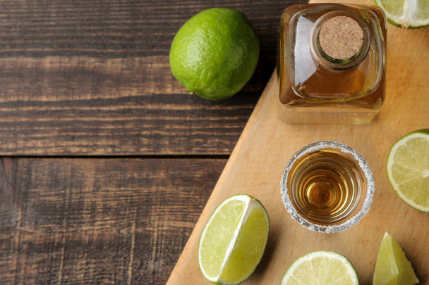tequila de oro en un vaso de vidrio con sal y lima sobre un fondo de madera marrón. vista superior con espacio para texto
 - Foto, Imagen