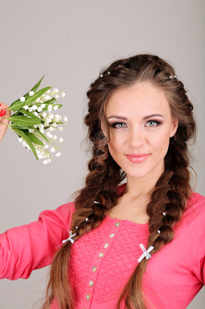 Young woman with beautiful hairstyle and flowers, on grey background - Φωτογραφία, εικόνα