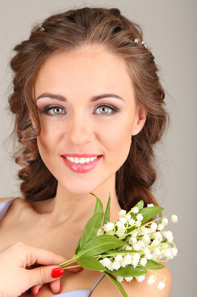 Young woman with beautiful hairstyle and flowers, on grey background - Фото, изображение
