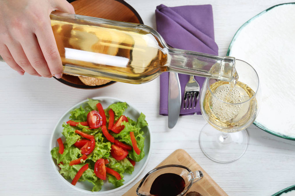 Woman pouring white wine into glass on table with delicious food, closeup - Φωτογραφία, εικόνα