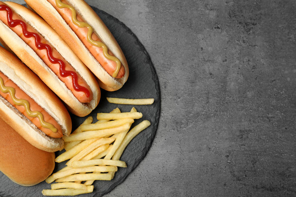Deliciosos cachorros-quentes e batatas fritas em fundo cinza, vista superior. Espaço para texto
 - Foto, Imagem