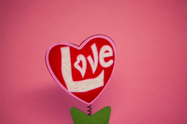 St. Valentine's Day. Red wooden heart with the inscription "love". On a spring with a clothespeg. As a flower in a pot. On a pink background. - 写真・画像