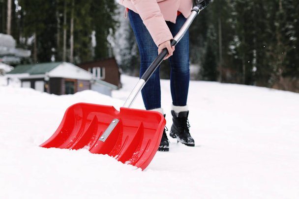 Woman removing snow with shovel near house - Foto, afbeelding