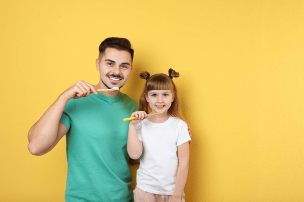 Little girl and her father brushing teeth together on color background, space for text - Foto, imagen