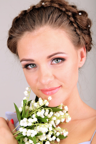 Young woman with beautiful hairstyle and flowers, on grey background - Фото, зображення