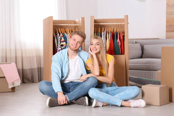Happy young couple sitting near wardrobe boxes indoors - Фото, изображение