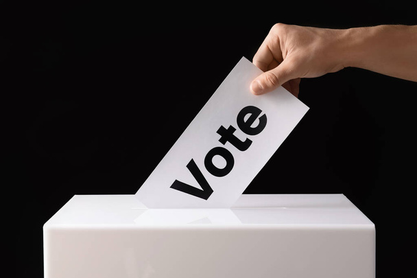 Man putting his vote into ballot box on black background, closeup - Photo, image