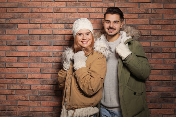 Casal jovem vestindo roupas quentes contra a parede de tijolo, espaço para texto. Pronto para férias de inverno
 - Foto, Imagem