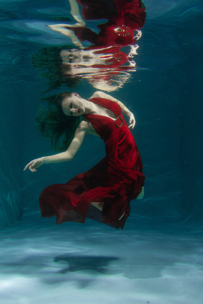 красивая свободная дайвер женщина плавает в длинном красном вечернем платье под водой в одиночку в глубокой
 - Фото, изображение