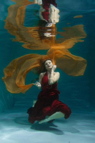 beautiful free diver woman swimming in long red evening dress under water alone in the deep - Fotó, kép