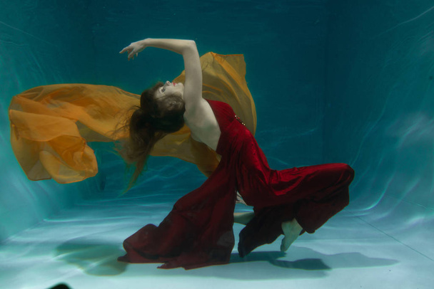 beautiful free diver woman swimming in long red evening dress under water alone in the deep - Foto, Imagen
