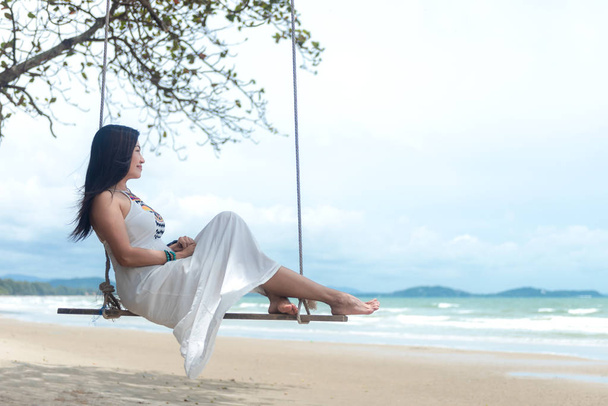 Summer Vacations. Lifestyle women relaxing and enjoying swing on the sand beach, fashion stunning women with white dress on the tropical island so happy and luxury in holiday summer. Travel and Summer Concept - Photo, Image