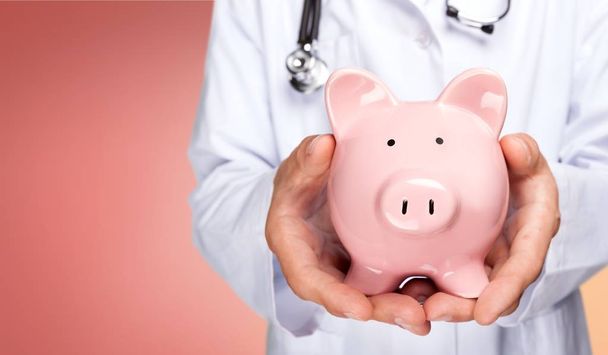 doctor with stethoscope holding pink piggy bank - Foto, afbeelding
