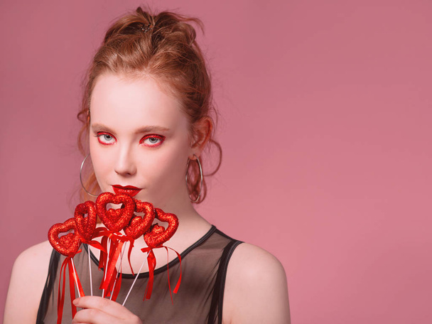 Portret van mooie aantrekkelijke stijlvolle jonge roodharige vrouw met make-up met saint valentine's day decoraties (harten) in haar handen met levende koraal toning - Foto, afbeelding