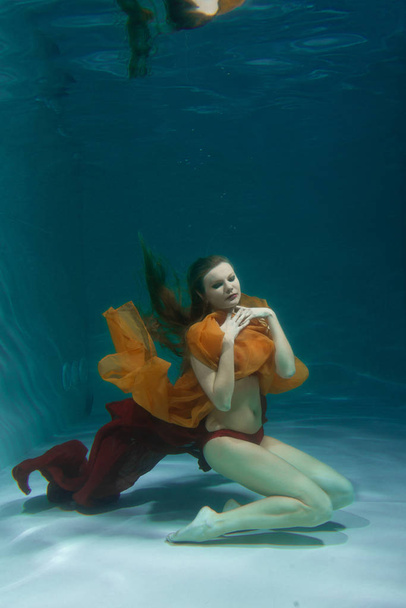 mooie Kaukasische lang haar vrouw onderwater zwemmen in rode sexy lingerie alleen in het diepe - Foto, afbeelding