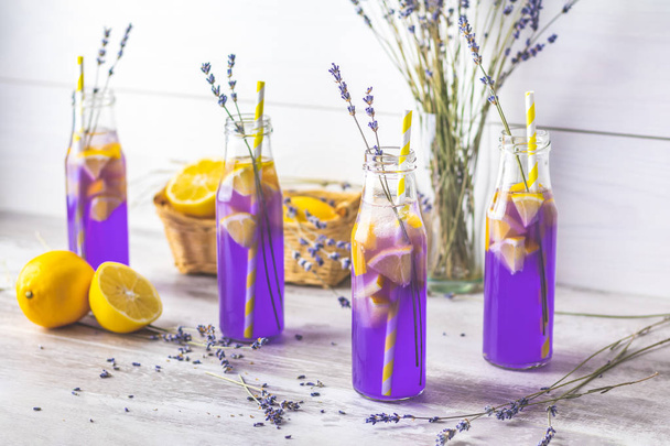 Свежий лавандовый фиолетовый коктейль с лимоном и льдом, стакан для питья бутылок на светлом старом деревенском стиле, выборочная фокусировка, мелкая глубина поля
. - Фото, изображение