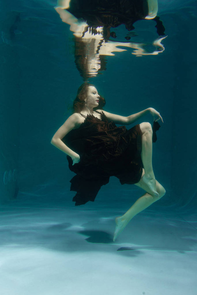 beautiful lady in long evening dress swimming underwater on the deep alone - Photo, Image