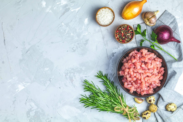 Homemade minced meat in a black bowl over light gray slate or stone or concrete background with ingredients for making. Top view with copy space. - Foto, Imagem