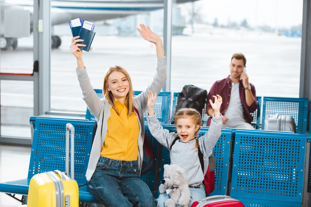 szelektív összpontosít cherful anya és lánya kezét feje fölött, és mosolyogva repülőtéren ember a háttérben - Fotó, kép
