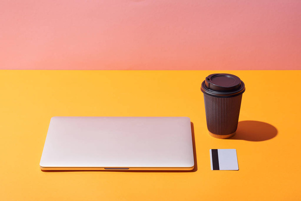 paper coffee cup near laptop and credit card on yellow surface and pink background - Photo, Image